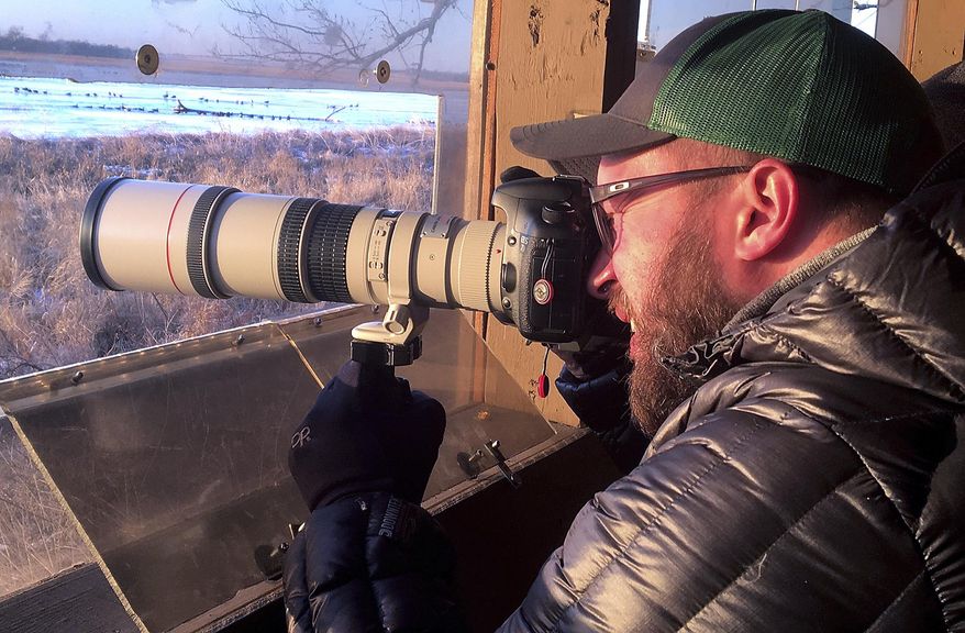 In this Thursday, March 28, 2019 photo, Morgan Dowdall , of Loveland, Colo., sets up his camera to catch a sandhill crane in action while on a guided tour at the Crane Trust Nature and Visitors Center south of Alda, Neb. The numbers were low on this visit because of the weather, and there were only about 3,000 cranes on the river instead of the usual 10,000 or more. (Robert Pore/The Independent via AP)