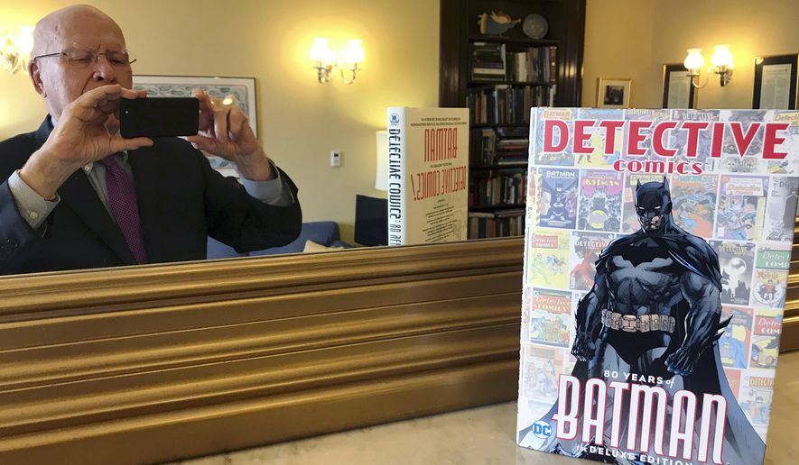 This Thursday, March 28, 2019, photo provided by Sen. Patrick Leahy, D-Vt., shows Leahy in a mirror and the 80th anniversary edition of a book commemorating the superhero Batman. Leahy, who wrote the forward for the book, has been a Batman fan since first reading the comic books as a child growing up in the 1940s in Montpelier, Vt. Leahy also has made brief appearances in a number of Batman movies. (Sen. Patrick Leahy via AP)