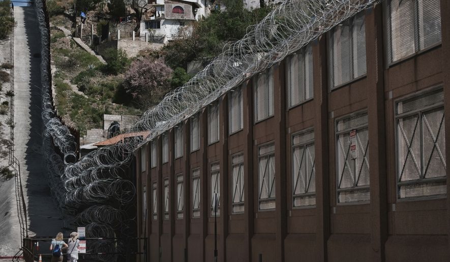 In this March 30, 2019 photo, a tourists take photos of the razor-wire-covered border wall that separates Nogalas, Ariz. at left, and Nogales, Mexico on the right. (AP Photo/Richard Vogel)