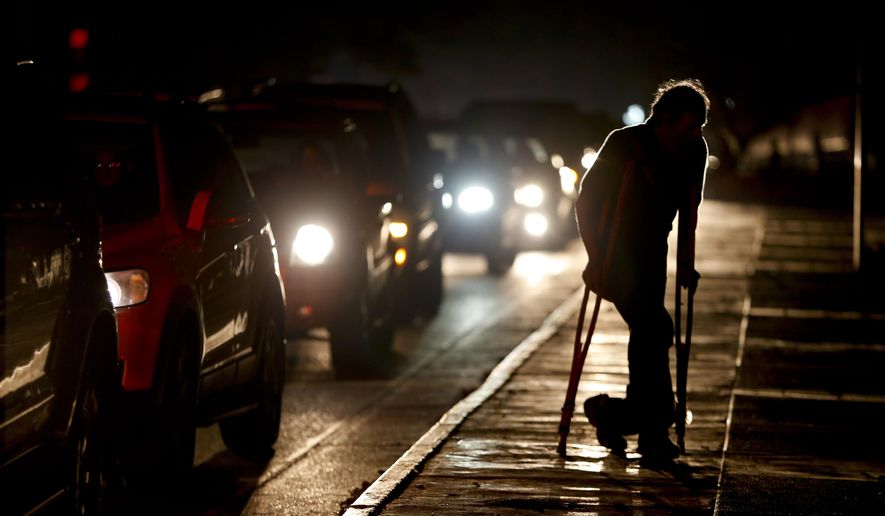 FILE - In this March 29, 2019 file photo, a man on crutches is illuminated by headlights of oncoming traffic, in Caracas, Venezuela. Venezuelans are struggling to understand the Sunday, March 31, 2019 announcement that the nation’s electricity is being rationed to combat daily blackouts. (AP Photo/Natacha Pisarenko, File)