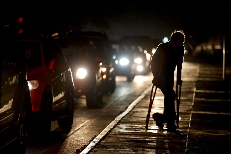 FILE - In this March 29, 2019 file photo, a man on crutches is illuminated by headlights of oncoming traffic, in Caracas, Venezuela. Venezuelans are struggling to understand the Sunday, March 31, 2019 announcement that the nation’s electricity is being rationed to combat daily blackouts. (AP Photo/Natacha Pisarenko, File)