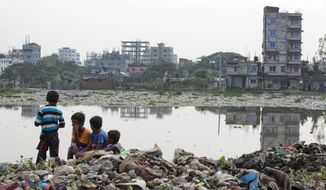 FILE - In this June 4, 2018, file photo, Bangladeshi children sit on garbage piled up by the river Buriganga in Hazaribagh area in Dhaka, Bangladesh. A new report by the United Nations children’s agency says the lives and futures of more than 19 million Bangladeshi children are at risk from colossal impacts of devastating floods, cyclones and other environmental disasters linked to climate change. The UNICEF report released Friday, April 5, 2019 said the tally includes Rohingya refugee children from Myanmar who are living in squalid camps in southern Bangladesh.( AP Photo/A.M. Ahad, File)