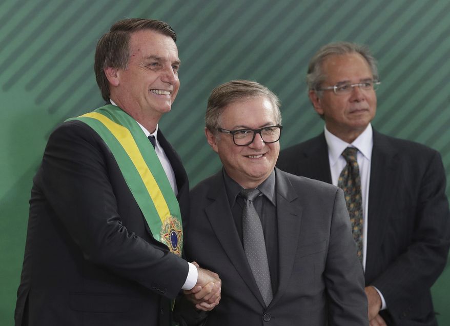 In this Jan. 1, 2019 photo, Brazil's President Jair Bolsonaro, left, shakes hands with Education Minister Ricardo Velez Rodriguez, during a swearing-in ceremony for his cabinet at the Planalto presidential palace, in Brasilia, Brazil. Velez Rodriguez said on Wednesday, April 3, 2019, that he will have school books revised to refer to the 1964 military coup as a “democratic regime by force.” (AP Photo/Eraldo Peres)