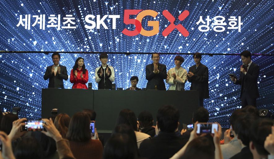 SK Telecom CEO Park Jung-ho, left, and participants attend a media showcase for its 5G service in Seoul, South Korea, Wednesday, April 3, 2019. SK Telecom will be launching commercial 5G services nationwide on Friday, April 5, in line with its competitors. The signs read: "The world's first commercial services." (AP Photo/Ahn Young-joon)