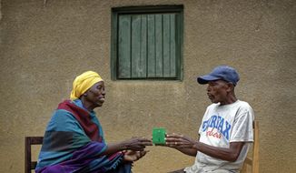 In this photo taken Thursday, April 4, 2019, genocide survivor Laurencia Mukalemera, left, a Tutsi, is offered a cup of water by Tasian Nkundiye, right, a Hutu who murdered her husband and spent eight years in prison for the killing and other crimes, before being interviewed at Nkundiye&#39;s home in the reconciliation village of Mbyo, near Nyamata, in Rwanda. Twenty-five years after the genocide the country has six &amp;quot;reconciliation villages&amp;quot; where convicted perpetrators who have been released from prison after publicly apologizing for their crimes live side by side with genocide survivors who have professed forgiveness. (AP Photo/Ben Curtis)
