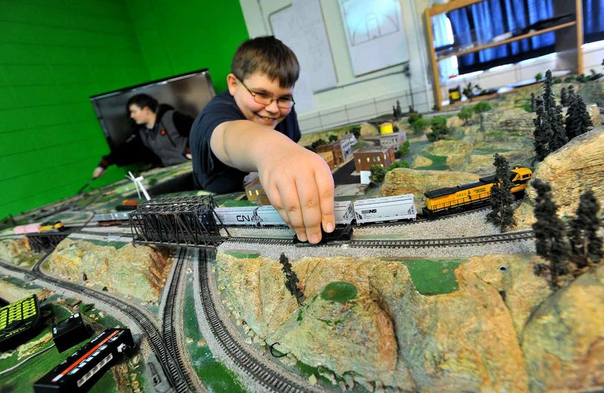 In this March 29, 2019, photo, Southeast Valley Middle School train club member Nykolas Albrecht, 11, cleans a section of track on their layout as fellow club member Emilie High, 13, left, works on another section in Burnside, Iowa. Students in the school operate a model railroad that's part of its model train club. (Hans Madsen/The Messenger via AP)
