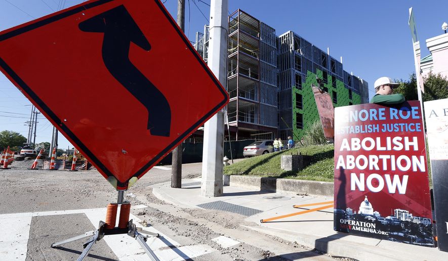 Abortion opponents stand outside the Jackson Women's Health Organization clinic, right, while construction on a hotel, background, continues in Jackson, Miss., Wednesday, April 10, 2019. The clinic is the only medical facility that performs abortions in the state. The state legislature recently passed a law that would ban most abortions after a fetal heartbeat is detected, meaning as early as six weeks. (AP Photo/Rogelio V. Solis)