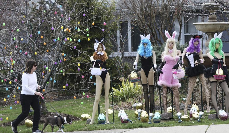A woman walks her dog past an Easter display in Clifton, N.J., Monday, April, 8, 2019. A New Jersey woman unhappy with her neighbor's racy Easter display used some garden shears to damage it. But the display's owner says it will soon be back up. The display at a dental office in Clifton featured five mannequins dressed in lingerie, all holding Easter baskets and surrounded by Easter eggs. It had drawn mixed reviews from neighbors, as well as passers-by who stopped to take photos. (Kevin R. Wexler/The Record via AP)