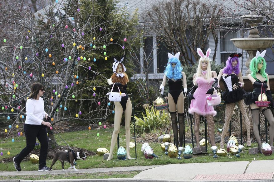 A woman walks her dog past an Easter display in Clifton, N.J., Monday, April, 8, 2019. A New Jersey woman unhappy with her neighbor's racy Easter display used some garden shears to damage it. But the display's owner says it will soon be back up. The display at a dental office in Clifton featured five mannequins dressed in lingerie, all holding Easter baskets and surrounded by Easter eggs. It had drawn mixed reviews from neighbors, as well as passers-by who stopped to take photos. (Kevin R. Wexler/The Record via AP)