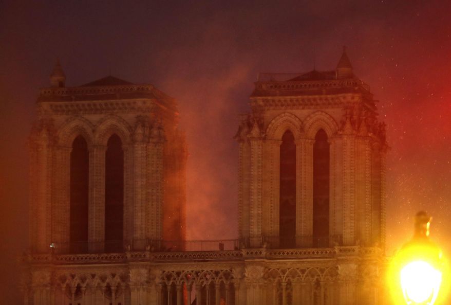 Flames illuminate the night sky as Notre Dame cathedral burns in Paris, Monday, April 15, 2019. Massive plumes of yellow brown smoke is filling the air above Notre Dame Cathedral and ash is falling on tourists and others around the island that marks the center of Paris. (AP Photo/Thibault Camus)