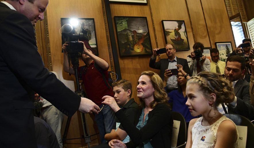 Colorado Gov. Jared Polis, left, hands a pen to Erin Martinez with her children Nathan, left from her, and Jaelynn, right, after signing Senate Bill 19-181 at the State Capitol in Denver, Tuesday, April 16, 2019. Polis signed into law a major overhaul of state oil and gas rules, shifting the focus away from encouraging production and directing regulators to make public safety and the environment their top priority. (Hyoung Chang/The Denver Post via AP)