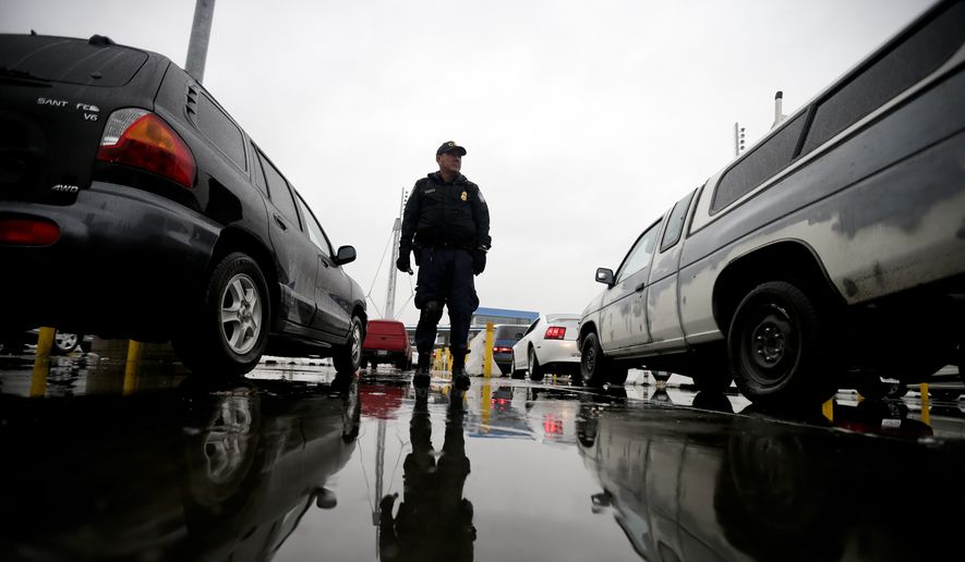 In this Dec. 3, 2014, file picture, an Immigration and Customs Enforcement (ICE) agent watches cars as they wait to enter the United States from Tijuana, Mexico, through the San Ysidro port of entry in San Diego. (AP Photo/Gregory Bull) ** FILE **