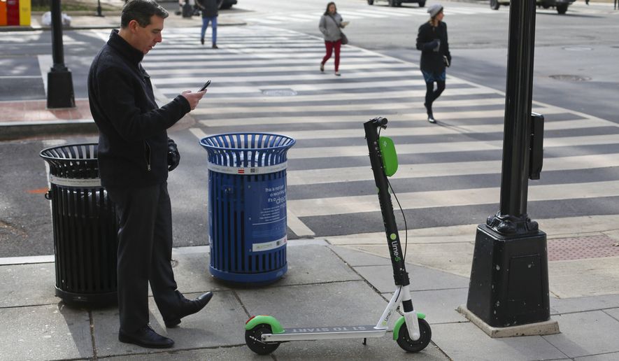 In this Dec. 6, 2018, photo a Lime scooter customer uses his mobile app to lock up his scooter on the sidewalk after finishing his trip in downtown Washington. (AP Photo/Pablo Martinez Monsivais)