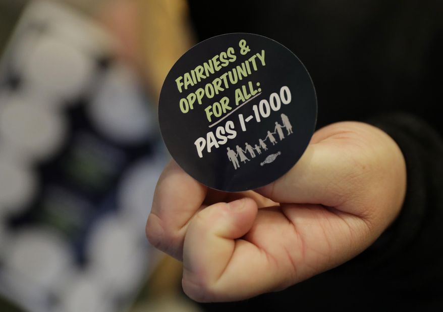 A volunteer holds a sticker showing support for Initiative 1000 outside a joint Washington state House and Senate committee, Thursday, April 18, 2019, at the Capitol in Olympia, Wash. Initiative 1000 would allow the state government to use affirmative action policies that do not constitute preferential treatment to remedy discrimination in public employment, education and contracting. (AP Photo/Ted S. Warren)
