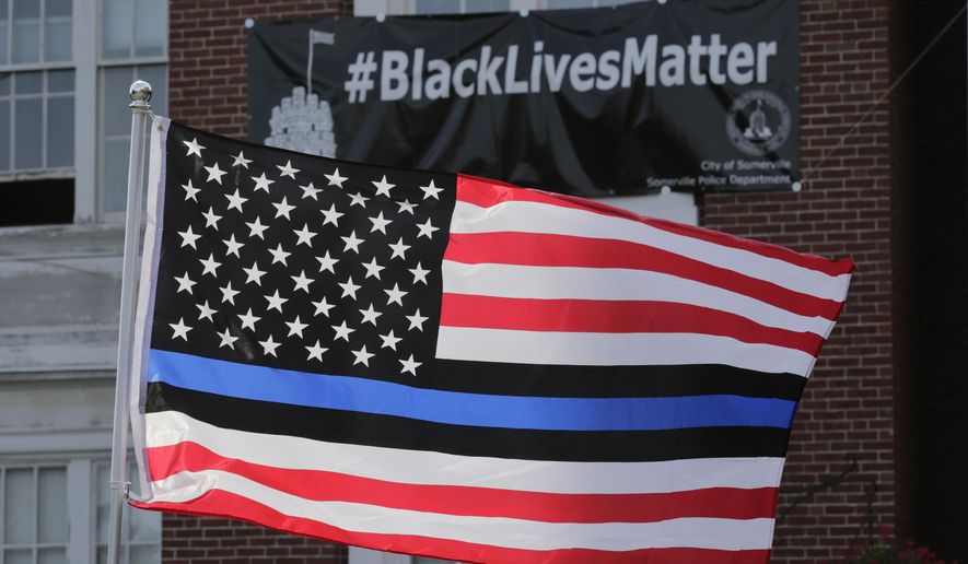 FILE - In this July 28, 2016, file photo, a flag with a blue and black stripes in support of law enforcement officers, flies at a protest by police and their supporters outside Somerville City Hall in Somerville, Mass. An Oregon county has agreed to pay $100,000 to a black employee who sued after a co-worker pinned up a "Blue Lives Matter" flag. The Oregonian/OregonLive reports Saturday, April 20, 2019, that Karimah Guion-Pledgure alleged in her January lawsuit that the flag demeans the "Black Live Matter" movement. (AP Photo/Charles Krupa, File)