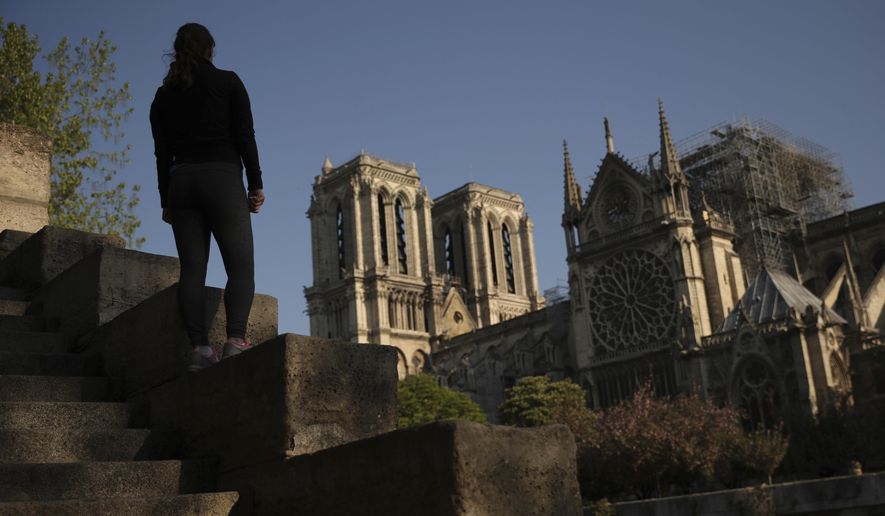 A woman stands on steps near the Notre Dame Cathedral in Paris, Saturday, April 20, 2019. Rebuilding Notre Dame, the 800-year-old Paris cathedral devastated by fire this week, will cost billions of dollars as architects, historians and artisans work to preserve the medieval landmark. (AP Photo/Francisco Seco)