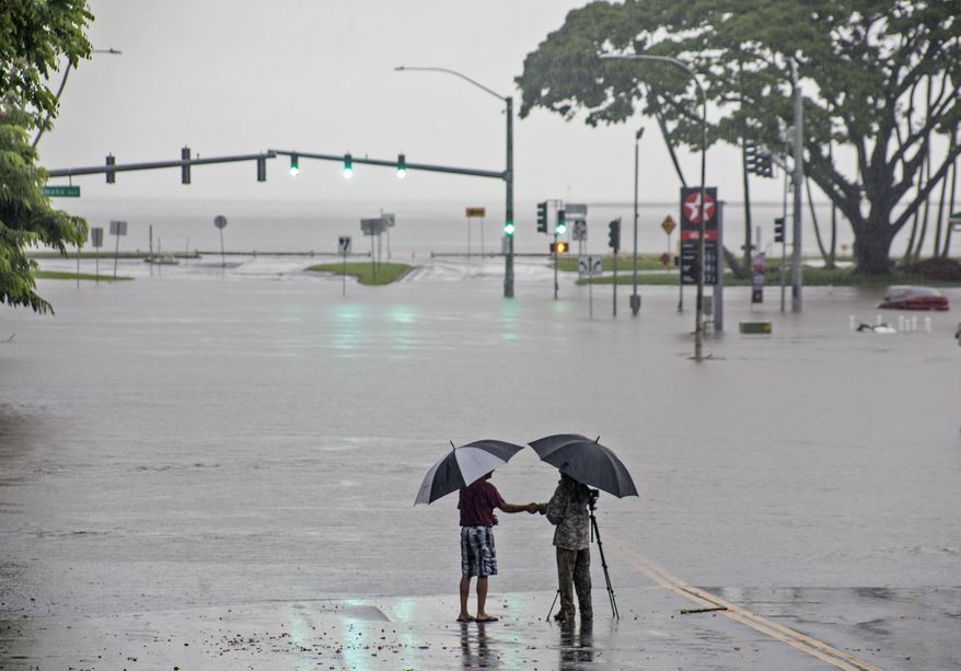 In this Aug. 23, 2018 file photo, people stand near flood waters from Hurricane Lane in Hilo, Hawaii. Some of Hawaii's most iconic beaches could soon be underwater as rising sea levels caused by global warming overtake its white sand beaches and bustling city streets. That’s alarming for a state where beach tourism is the primary economic driver. (Hollyn Johnson/Hawaii Tribune-Herald via AP, File)
