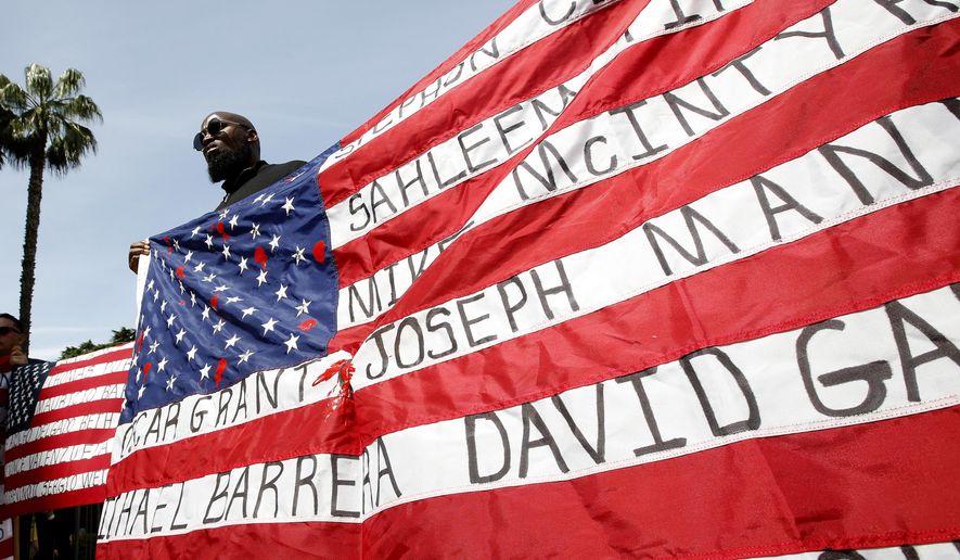 File - In this April 8, 2019, file photo, Malaki Seku Amen holds up an American flag with the names of people shot and killed by law enforcement officers, as he joins other in support of a bill that would restrict the use of deadly force by police in Sacramento, Calif. Round two is under way in California&#x27;s fight over how best to limit fatal shootings by police through nation-leading reforms. State legislators on Tuesday, April 23, 2019, are debating a measure that proponents say would set a national precedent by creating statewide guidelines on when officers can use lethal force and requiring that every officer be trained in ways to avoid opening fire. (AP Photo/Rich Pedroncelli, File)
