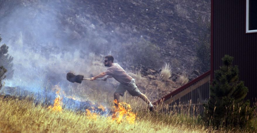 FILE - In this Aug. 14, 2012 file photo a man tosses dirt on a fire as he tries to save his home on Bettas Road near Cle Elum, Wash. Federal officials have released a plan to save sagebrush habitats in Western states that support cattle ranching, recreation and 350 wildlife species, including imperiled sage grouse. Officials say the 248-page document released this month is a paradigm shift relying on advances in technology and analytics to categorize sagebrush areas based on resistance and resilience to wildfire. (AP Photo/Elaine Thompson,File)