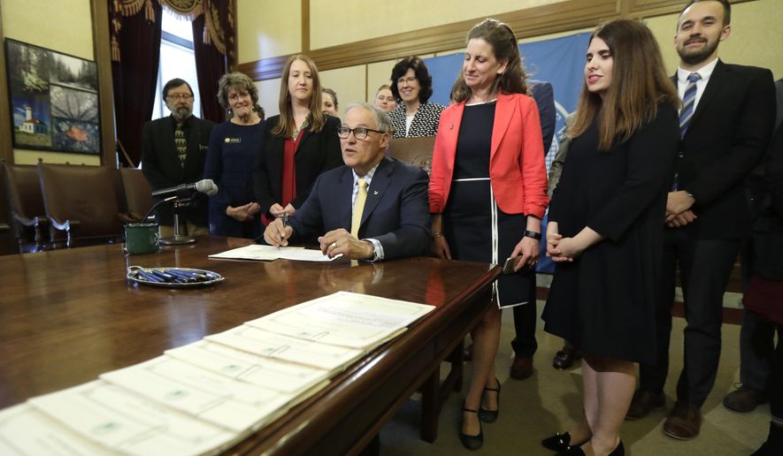 Washington Gov. Jay Inslee, seated center, makes remarks before signing a bill into law, Wednesday, April 24, 2019, at the Capitol in Olympia, Wash. The bill creates a new group of crimes reserved specifically for minors who are caught with explicit images of other minors, attempting to solve what lawmakers described as a paradox in current law, where even youth who report a sexual picture or video can themselves be potentially charged with a felony and even forced to register as sex offenders. (AP Photo/Ted S. Warren)
