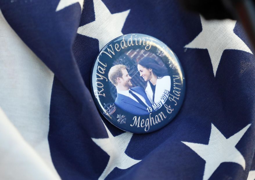 FILE- In this Thursday, May 17, 2018 file photo, a badge showing Prince Harry and Meghan Markle is pinned onto a US flag in Windsor, England. The child of Meghan Markle and Prince Harry will be seventh in the line of succession to the British throne, and also could be an American. The baby expected to arrive in the next few weeks would be the first citizen of Britain’s former colonies born into the upper echelons of the royal family. (AP Photo/Frank Augstein, File)