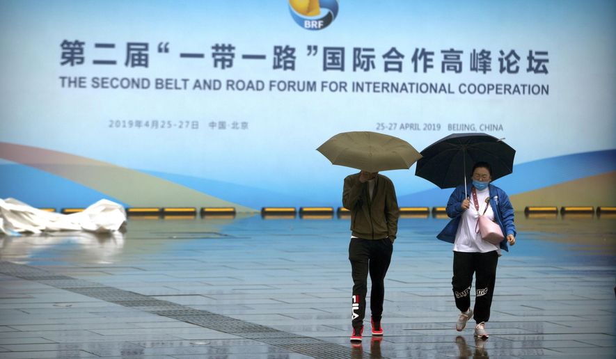 People carry umbrellas as they walk past a banner for the Belt and Road Forum at the China National Convention Center in Beijing, Saturday, April 27, 2019. (AP Photo/Mark Schiefelbein) **FILE**