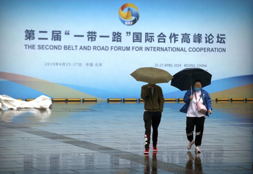People carry umbrellas as they walk past a banner for the Belt and Road Forum at the China National Convention Center in Beijing, Saturday, April 27, 2019. (AP Photo/Mark Schiefelbein) **FILE**