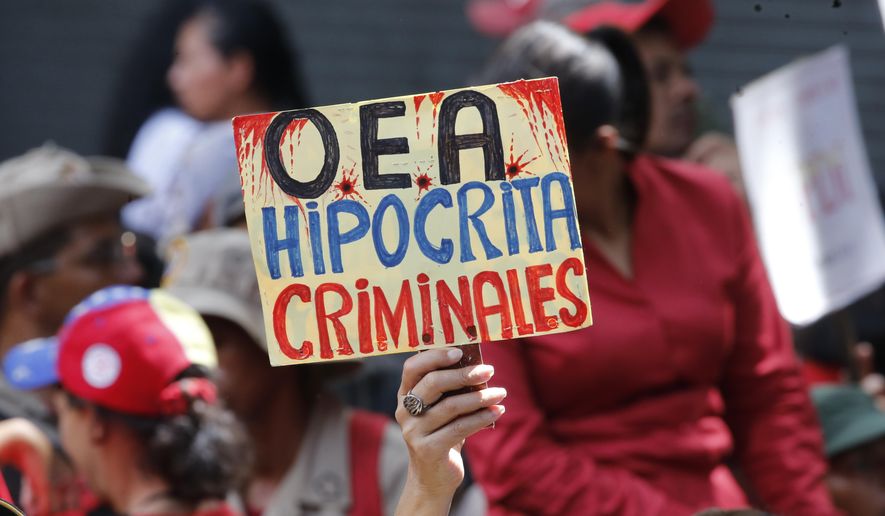A supporter of Venezuela&#39;s president Nicolas Maduro, holds a sign that reads in Spanish &amp;quot;OAS Hypocrites, Criminals&amp;quot; during a government rally in Caracas, Venezuela, Saturday, April 27, 2019. The Trump administration has added Venezuelan Foreign Minister Jorge Arreaza to a Treasury Department sanctions target list as it increases pressure on embattled President Nicolas Maduro. (AP Photo/Ariana Cubillos)