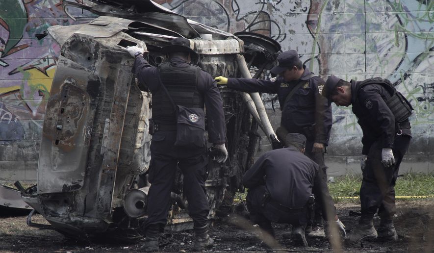 Police review the charred remains of a car that exploded as authorities were responding to a report of a vehicle with a corpse inside, in the San Bartolo neighborhood of Soyapango, El Salvador, Monday, April 29, 2019. Two police officers were injured in the explosion. (AP Photo/Salvador Melendez)