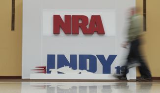 A visitor to the at the National Rifle Association Annual Meeting walks past signage for the event in Indianapolis, Saturday, April 27, 2019. (AP Photo/Michael Conroy)