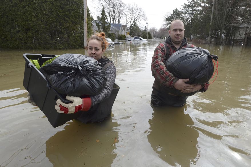 Residents Lawrence Courville, left, and Andy Goulet carry belongings down a flooded street in Ste-Marthe-sur-le-Lac, Quebec, Sunday, April 28, 2019. (Ryan Remiorz/The Canadian Press via AP)