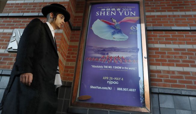 A young, Orthodox Jewish man dressed for the Passover holiday walks to the New Jersey Center for the Performing Arts, Wednesday, April 24, 2019, in Newark, N.J., before the start of a Yiddish performance, as he passes a poster advertising Shen Yun. During a limited engagement, the performing arts center will host Shen Yun, Falun Gong&#x27;s high-flying, globe-trotting dance troupe, which has been banned from China as a cult. (AP Photo/Kathy Willens)