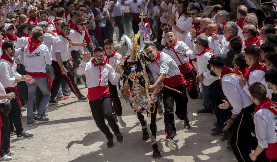 In this Thursday, May 2, 2019 photo, a troupe and their richly decorated horse make their way amid the crowd during the "Los Caballos del Vino," usually translated as the Running of the Wine Horses in Caravaca de la Cruz, southeast Spain. The annual fiesta is said to date from the 13th century when the Knights Templar broke a siege. The colorful spectacle draws thousands of tourists. (AP Photo/Bernat Armangue)