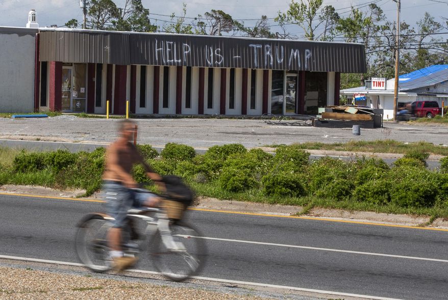 In this May 3, 2019 photo, a cyclist rides by a building damaged by Hurricane Michael in Parker, Fla. Residents in these parts of the Florida Panhandle that were devastated by Hurricane Michael six months ago hope President Donald Trump gets a glimpse of the continuing suffering in the region when he arrives for a campaign rally this week. (AP Photo/Mike Fender)
