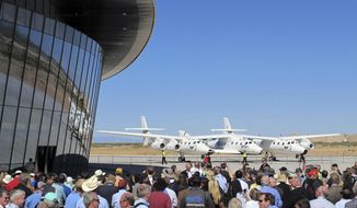 FILE - In this Oct. 17, 2011, file photo a crowd gathers outside Spaceport America for a dedication ceremony as Virgin Galactic&#39;s mothership WhiteKnightTwo sits on the tarmac near Upham, N.M. British billionaire Richard Branson is taking another concrete step toward offering rides into the close reaches of space for paying passengers. Branson announced Friday, May 10, 2019, that Virgin Galactic will immediately begin shifting operations from California to a spaceport and specialized runway in the New Mexico desert in final preparations for commercial flights. He says Virgin Galactic&#39;s development and testing program has advanced enough to make the move, which will continue through the summer. (AP Photo/Susan Montoya Bryan, File)