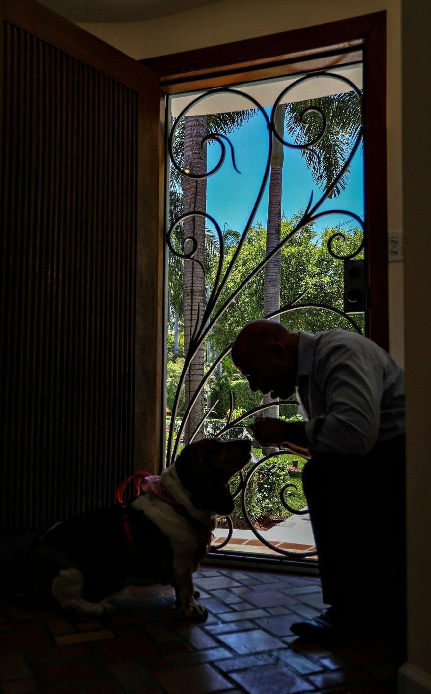 Richard Silverman gives snacks to his basset hound, "Daisy", inside his Mediterranean Revival home. Some Miami Beach Palm View neighborhood residents gathered at the home of Richard Silverman to discuss their fight to remove the historic designation of the South Beach neighborhood on Tuesday, April 23, 2019. (Carl Juste/Miami Herald via AP)