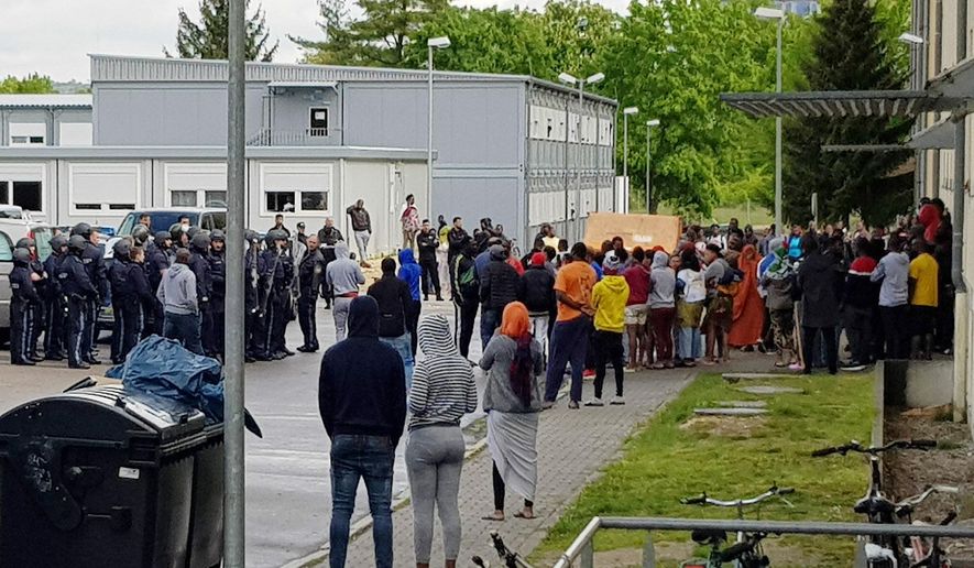 German police officers and migrants stand in front of an asylum center after a woman was found dead in the center in Regensburg, Germany, Saturday, May 11, 2019. German police say it took them several hours to recover the body of the 31-year-old African woman from the center because angry residents there pelted officers with stones and other objects. (Alexander Auer/dpa via AP)