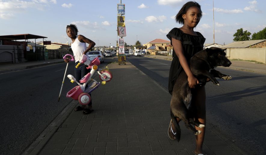 A young girl carries her dog as she crosses the main road, with headline from a newspaper and election posters on the streets of Soweto, South Africa, Friday, May 10, 2019. The ruling African National Congress is coasting to a comfortable lead in South Africa&#39;s presidential and parliamentary elections with 80% of the vote counted, but the ongoing tally shows the party getting less support than in the previous poll five years ago. (AP Photo/Themba Hadebe)