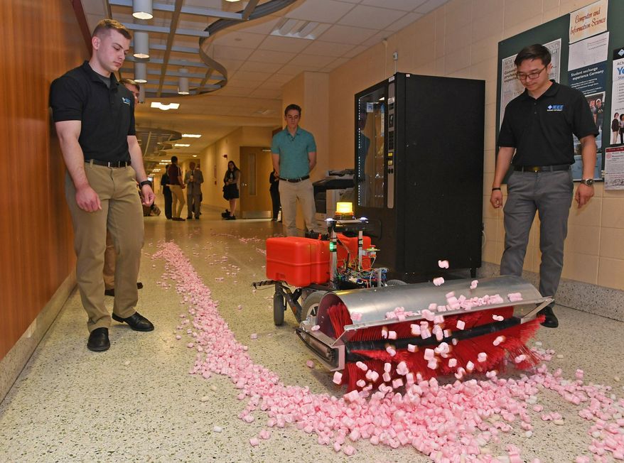 From left: Niklas Bitters, 22; Mitch Wesley, 22; and Tenger Batjargal, 23, watch as an autonomous snow-removal robot moves along a hallway at the Zurn Science Center at Gannon University in Erie, Pa., on May 10, 2019. The Gannon engineering students were part of a team that built the robot during the 2018-19 school year as their senior project, which they presented to faculty on May 10, 2019. The robot is programmed with a route and then sensors keep it on that route. The team says this machine has 16 miles of battery life and can sweep up to four inches of snow. (Christopher Millette/Erie Times-News via AP)