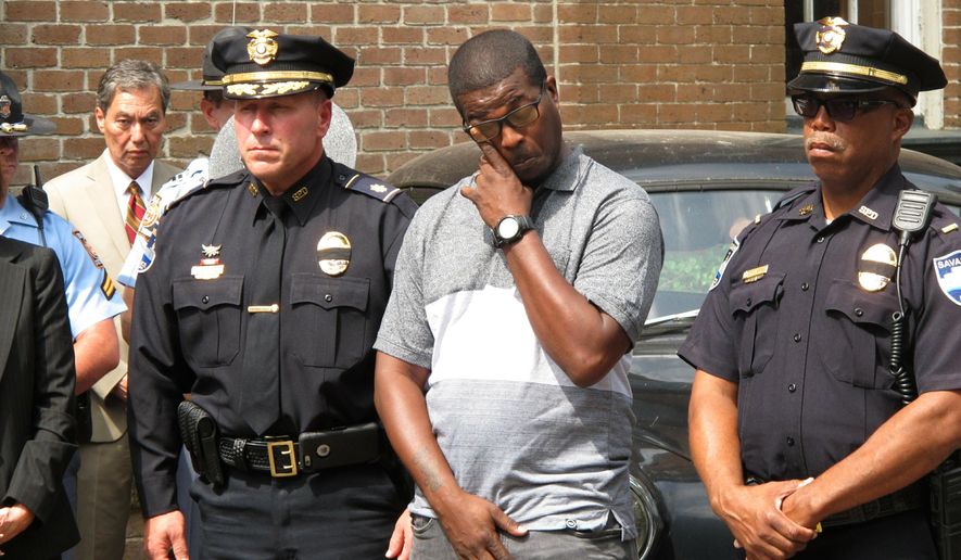 Savannah police Officer Douglas Thomas, center in plain clothes, wipes an eye as he stands between police Maj. Robert Gavin, left, and Lt. Gregory Mitchell, during a memorial event Monday, May 13, 2019, for an officer killed in a weekend shooting. Authorities say Thomas was wounded in the leg and Sgt. Kelvin Ansari was fatally shot while responding to an armed robbery call Saturday, May 11, 2019. The suspect, Edward Fuller III, was shot and killed by police. (AP Photo/Russ Bynum)