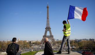 FILE - In this Saturday, March 30, 2019 file photo, a man holds a French flag as French with the Eiffel Tower in the background, during protests in Paris. Paris is wishing the Eiffel Tower a happy birthday with an elaborate laser show retracing the monument&#x27;s 130-year history. First, the monument invited 1,300 children to a giant &amp;quot;snack time&amp;quot; Wednesday, May 15 beneath the tower dubbed the Iron Lady. (AP Photo/Thibault Camus, file)
