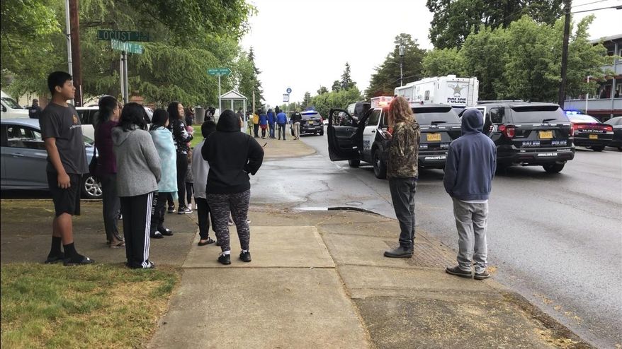 Bystanders on gather on a street corner and look at police activity following the shooting and wounding of a Salem policewoman on Wednesday, May 15, 2019, in Salem, Ore. The policewoman was treated and released from a hospital for multiple gunshot bones, and the suspect was taken into custody.(AP Photo/Andrew Selsky)