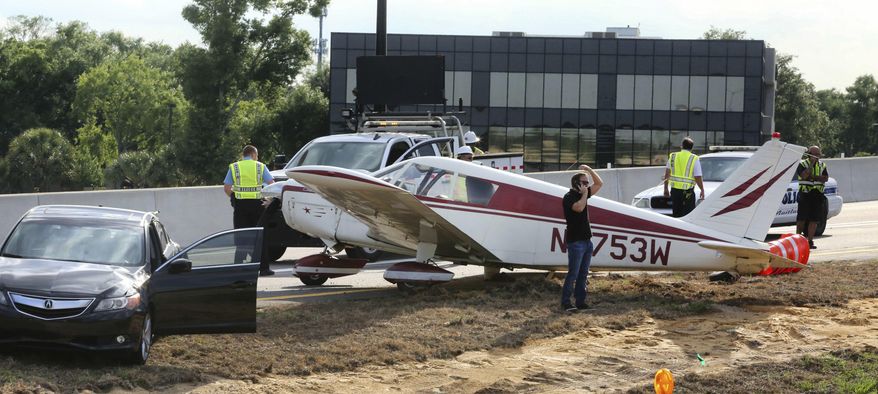 A driver, center, of a black Acura, far left, talks on a cell phone after the vehicle was struck by a small plane making a crash landing on the eastbound ramp of Maitland Blvd. to Interstate 4, Thursday, May 16, 2019, in Maitland, Fla. (Joe Burbank/Orlando Sentinel via AP)