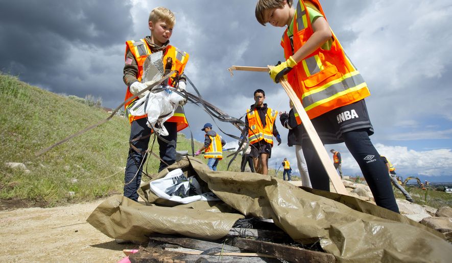 In a Wednesday, May 8, 2019 photo, Brenton Cramer, 10, left, and Damon Haub, 10, both of Lehi, gather trash into a pile as he and other volunteers help to complete an Eagle Scout Service Project that aims to create a walkable path connecting nearby neighborhoods to Ignite Entrepreneurship Academy and a future park, just northwest of the charter school in Lehi, Utah. (Isaac Hale/The Daily Herald via AP)