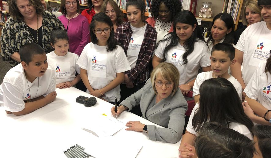 FILE - In this April 3, 2019 file photo, New Mexico Gov. Michelle Lujan Grisham, seated, with pen, signs legislation to raise teacher salaries and increase annual spending on public schools by almost a half-billion dollars at Salazar Elementary School in Santa Fe, N.M. New Mexico school districts have become increasingly reliant on substitutes as they contend with growing vacant teaching positions in the state. (AP Photo/Morgan Lee, File)