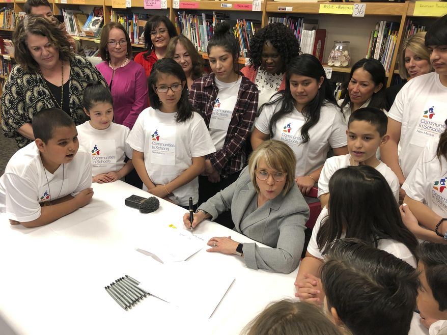 FILE - In this April 3, 2019 file photo, New Mexico Gov. Michelle Lujan Grisham, seated, with pen, signs legislation to raise teacher salaries and increase annual spending on public schools by almost a half-billion dollars at Salazar Elementary School in Santa Fe, N.M. New Mexico school districts have become increasingly reliant on substitutes as they contend with growing vacant teaching positions in the state. (AP Photo/Morgan Lee, File)