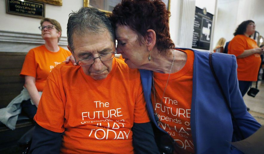 Mary Ann DeMello hugs her husband Frank, who has Alzheimer's disease, during a rally at the Statehouse in Boston, Tuesday, May 21, 2019. Advocates gathered as the Massachusetts Senate began debating its version of a proposed $42.7 billion state budget. (AP Photo/Michael Dwyer)