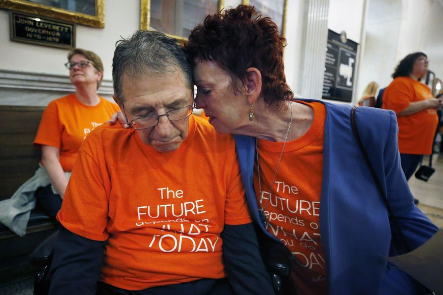 Mary Ann DeMello hugs her husband Frank, who has Alzheimer's disease, during a rally at the Statehouse in Boston, Tuesday, May 21, 2019. Advocates gathered as the Massachusetts Senate began debating its version of a proposed $42.7 billion state budget. (AP Photo/Michael Dwyer)
