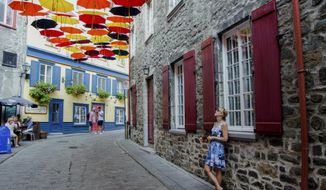 Paule Bergeron takes in the scene in Place-Royale in Old Quebec, Aug. 27, 2018. Quebec City offers compelling urban bike routes along the river, out to Montmorency Falls and through intriguing neighborhoods, as well as access to the Jacques-Cartier rail trail running through forest, farmland and meadows. (AP Photo/Cal Woodward)
