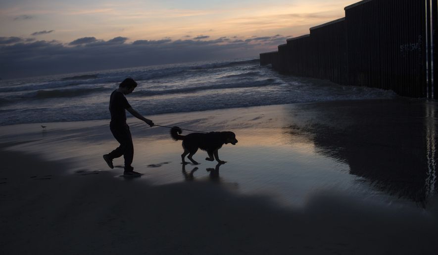 A man and his dog are silhouetted against an early evening landscape while walking along a Pacific Ocean shore, near the U.S. border fence that separates Tijuana, Mexico from San Diego, Calif., Tuesday, April 4, 2017. (AP Photo/Rodrigo Abd)